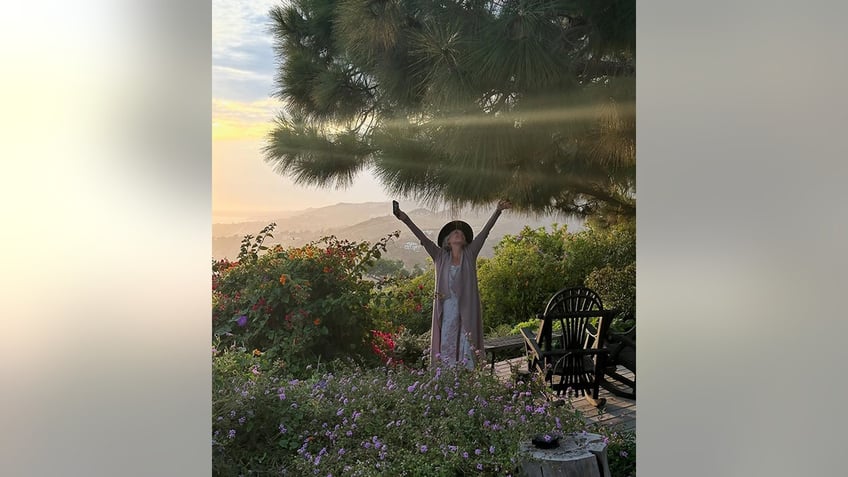 Ricki Lake raises her arms on her Malibu property with a sunset in the background