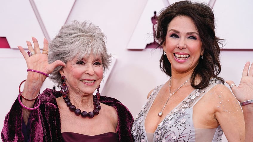 Rita Moreno in a plum colored dress and shall waves at the Academy Awards with daughter Fernanda