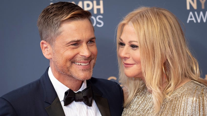 Rob Lowe in a tuxedo smiles as his wife Sheryl in a sparkly dress looks at him lovingly