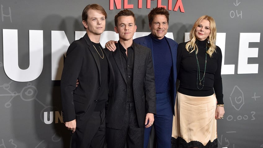 Matthew Lowe in a black suit stands next to John Owen Lowe in a black suit next to father Rob Lowe in a blue shirt and fitted suit next to wife Sheryl in a black top and khaki colored skirt on the red carpet for "Unstable"