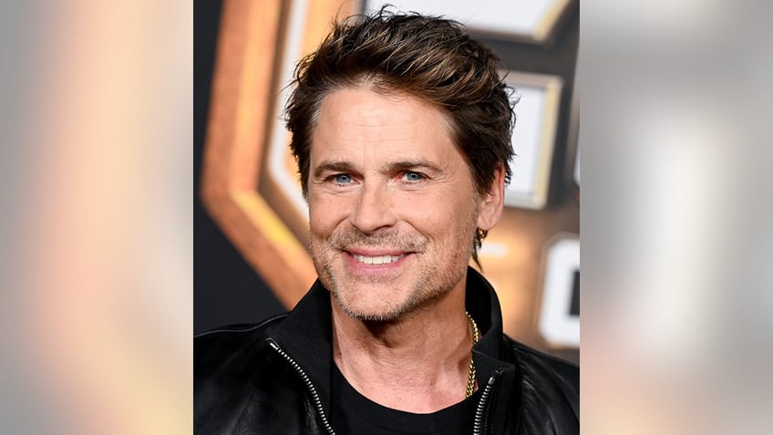 Rob Lowe smiles directly at the camera in a black jacket on the red carpet of "Guardians of the Galaxy Vol. 3"