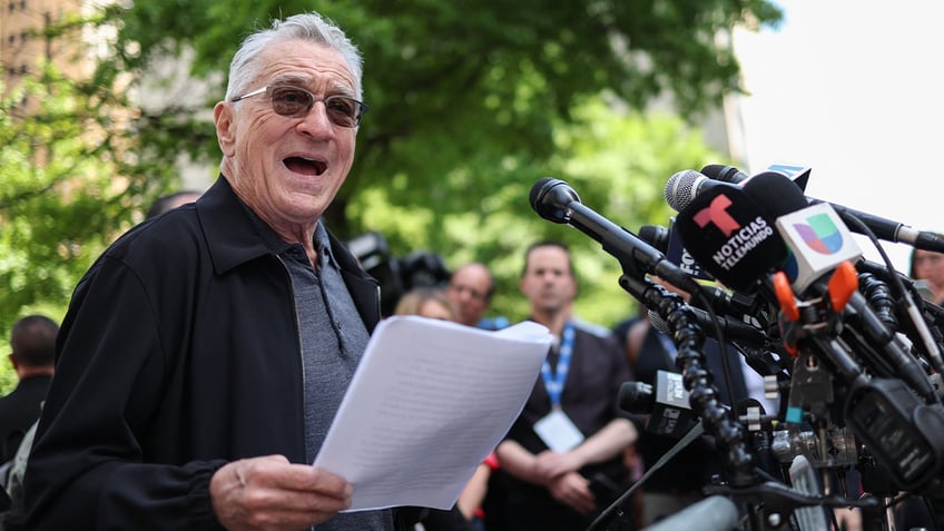 Robert De Niro at bank of microphones in outdoor press conference