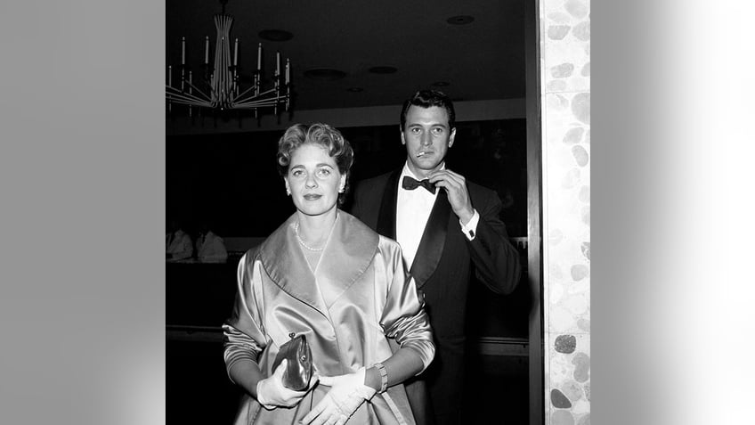 Rock Hudson walking behind his wife Phyllis Gates while smoking a cigarette