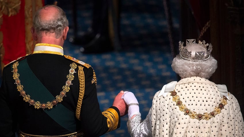 King Charles and Queen Elizabeth with their backs turned in royal robes holding each other's hands