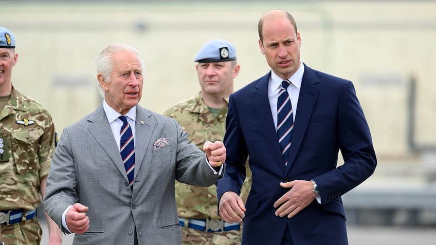 King Charles wearing a grey suit walking next to Prince William in a navy suit