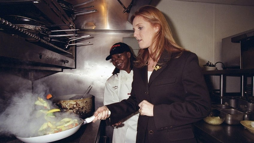 Sarah Ferguson in a dark brown blazer cooking in a kitchen.