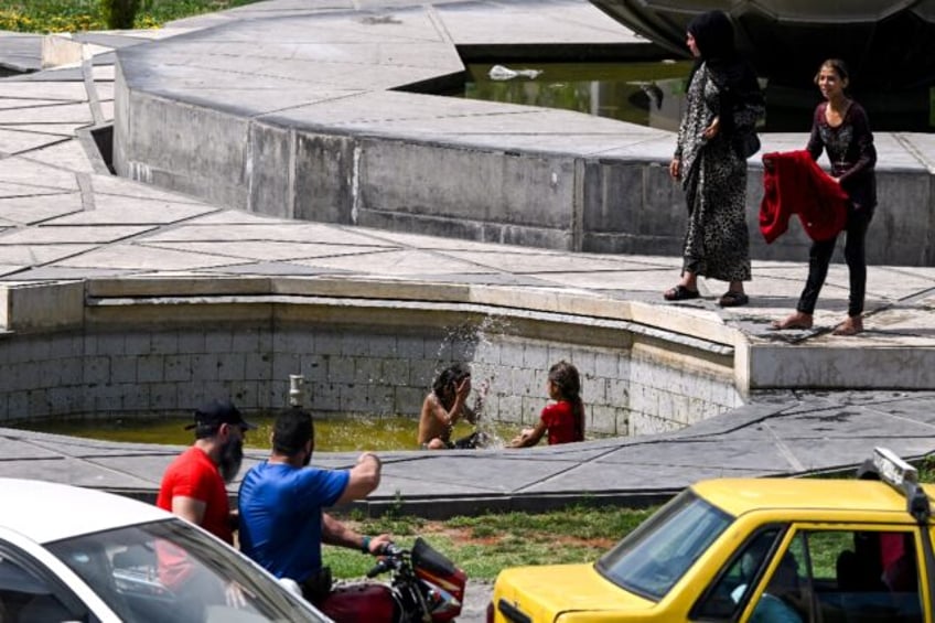 Motorists drive past as Syrian children play at a water fountain in Sabaa Bahrat Square in