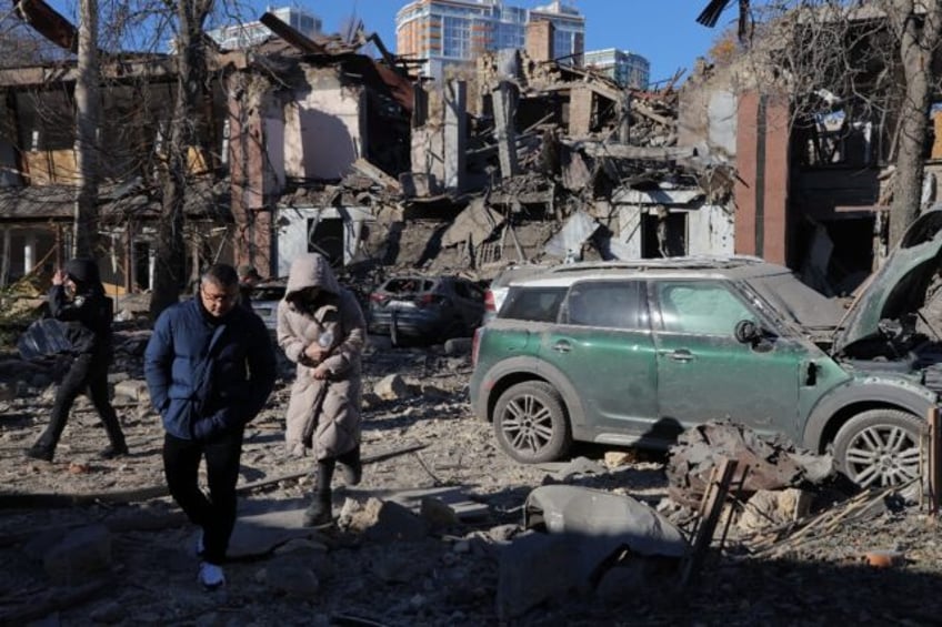 Local residents and police walk next to damaged cars and a destroyed building following a