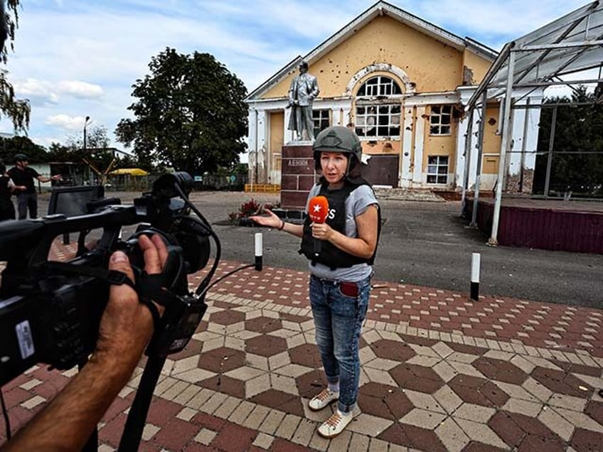 Ukrainian TV journalists work in front of a building and a monument to Vladimir Lenin dama