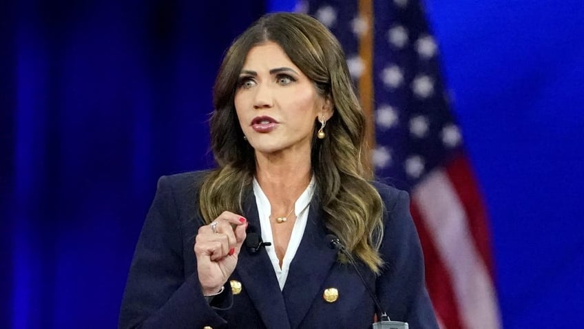 closeup shot of Kristi Noem, U.S. flag behind her