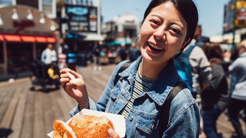 A woman is all smiles as she eats clam chowder in a sourdough bread bowl in San Francisco.