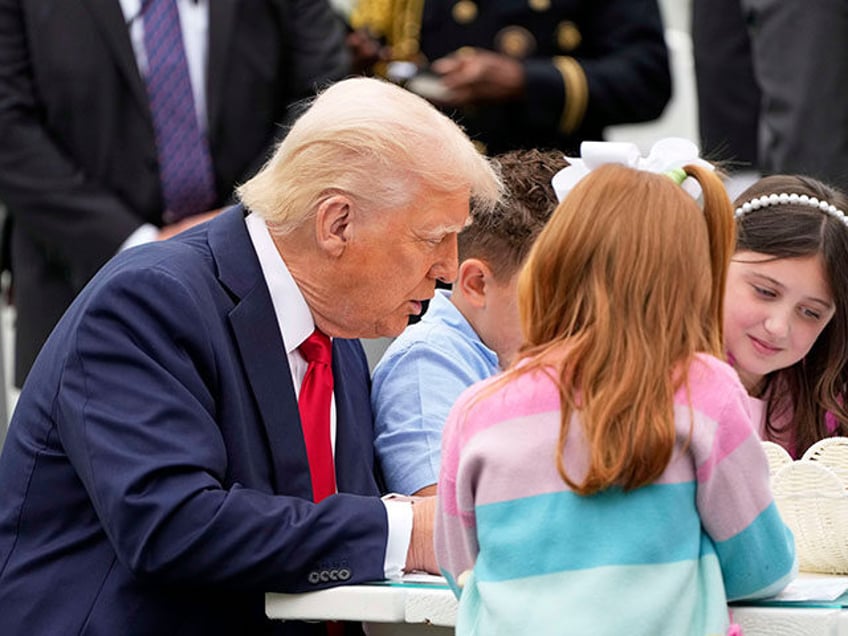President Donald Trump sits with children as he participates in the White House Easter Egg