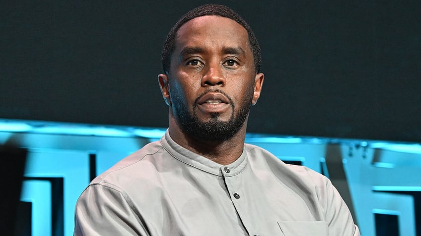 Sean Combs sits on stage in a grey shirt and looks invested in a conversation
