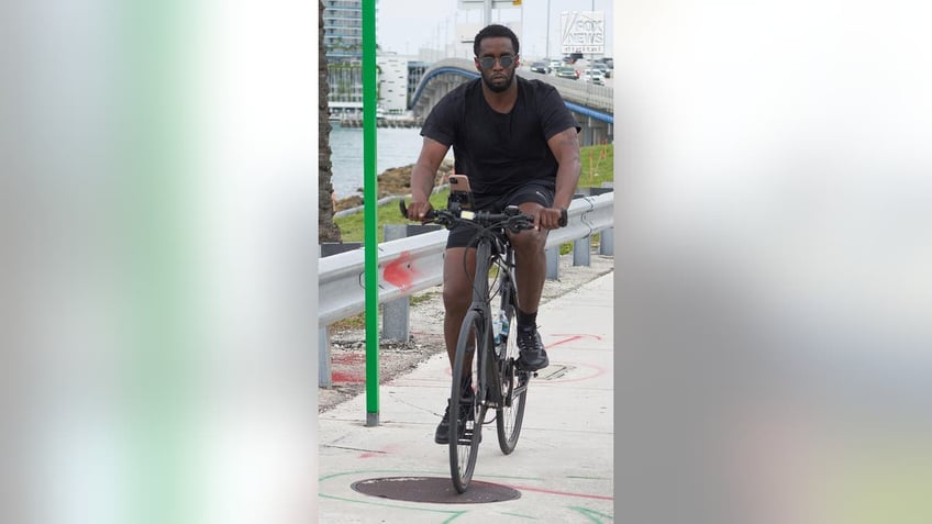 P Diddy looks at the camera wearing sunglasses as he rides his bicycle.