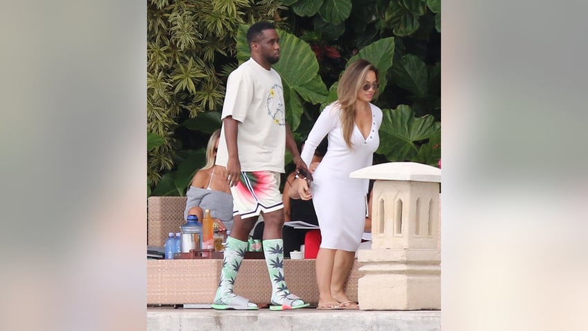 Diddy in a white shirt and white, red and green shorts walks alongside Daphne Joy in a white dress in Miami Beach