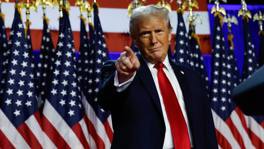 Trump points at supporters while standing in front of a row of US flags