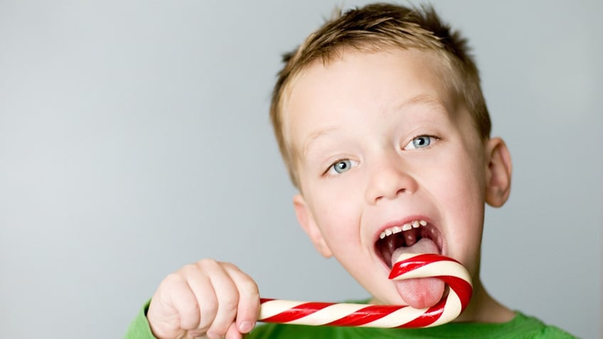 A boy licks a giant candy cane.