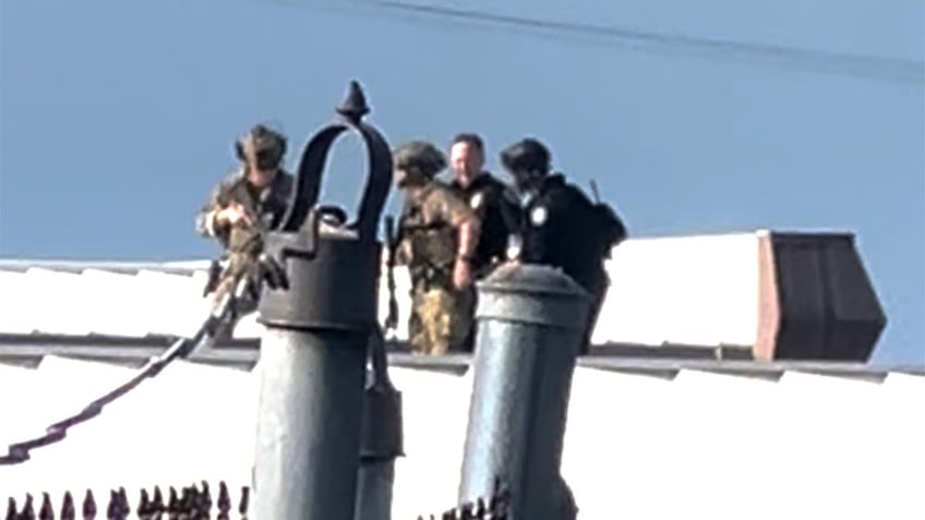 Law enforcement officers stand over the body of would-be Trump assassin, Thomas Crooks on the roof of a building