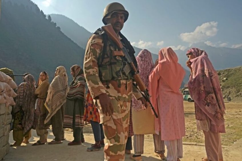 A security personnel stands guard as voters queue up to cast their ballots in Indian-admin