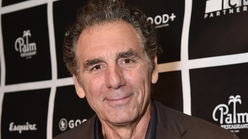 Michael Richards soft smiles on the carpet in a brown coat