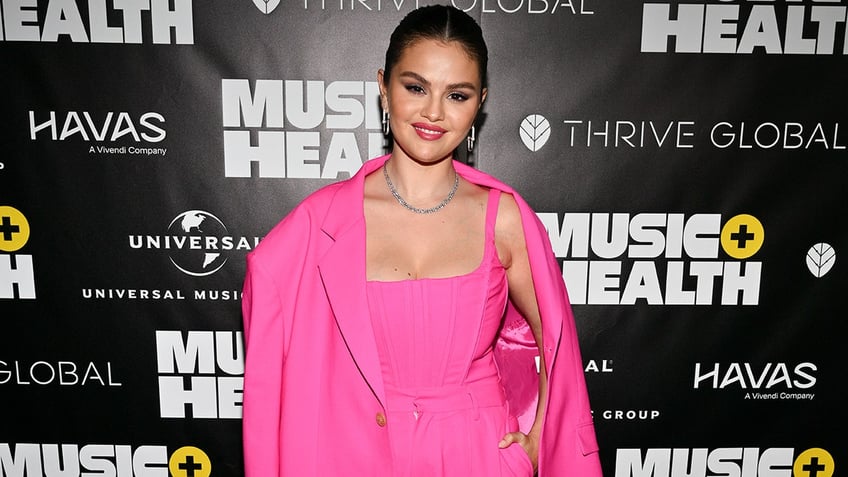 Selena Gomez in a hot pink corset top and matching pink blazer and pants smiles on the carpet