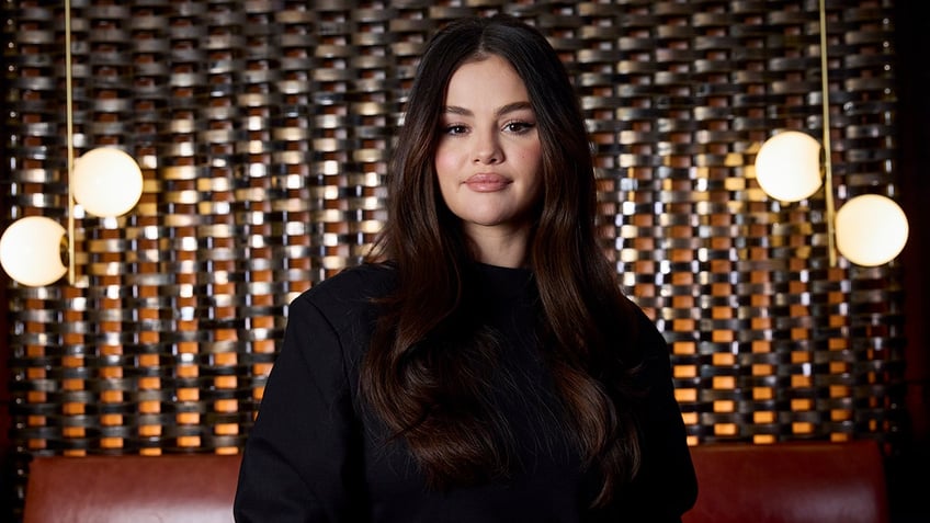 Selena Gomez in a black dress looks directly at the camera with lights set up behind her