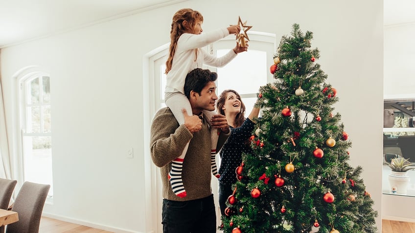 Little girl putting the star on top of the Christmas tree