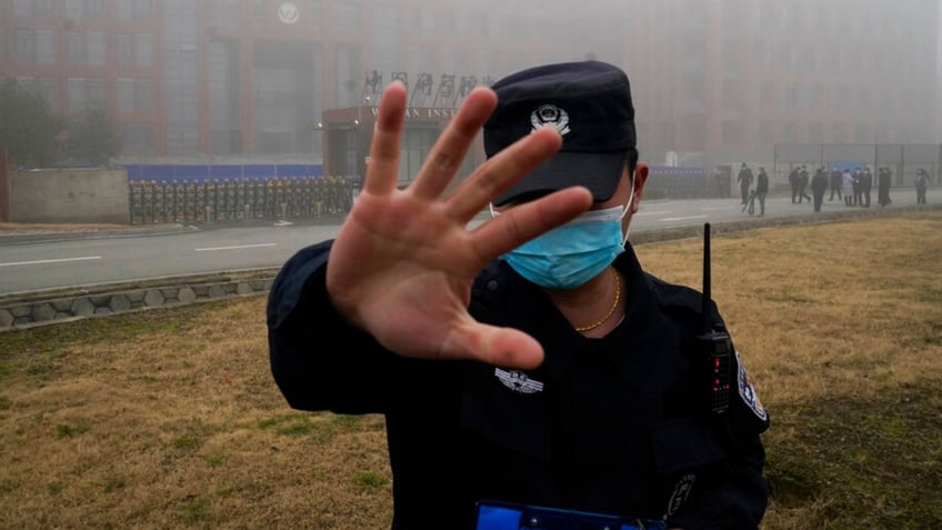 A security person moves journalists away from the Wuhan Institute of Virology