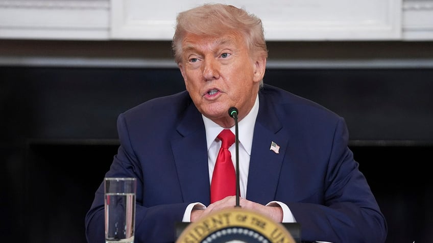 President Donald Trump wearing red tie, sitting as he speaks