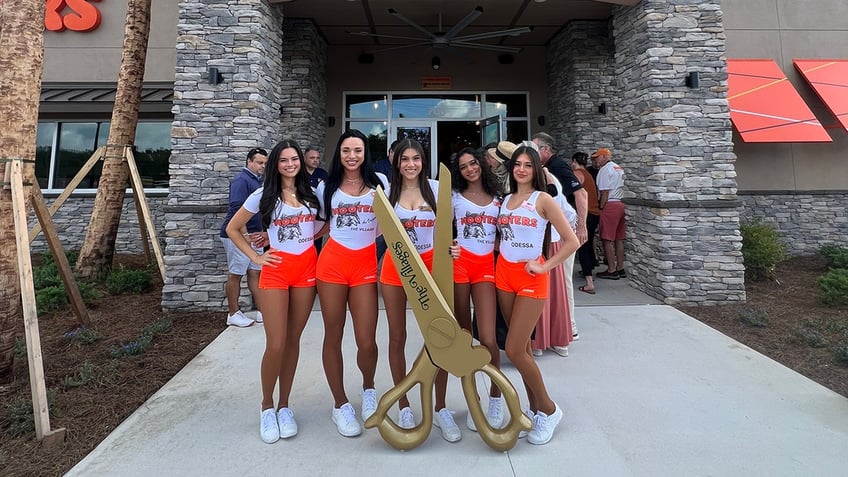 Five Hooters waitresses stand in front of a giant pair of scissors for the grand opening of The Villages, Florida, location.