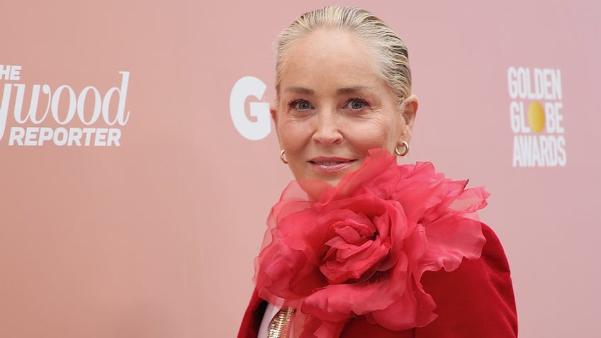 Sharon Stone looks at the camera in a red jacket with a large flower on the shoulder