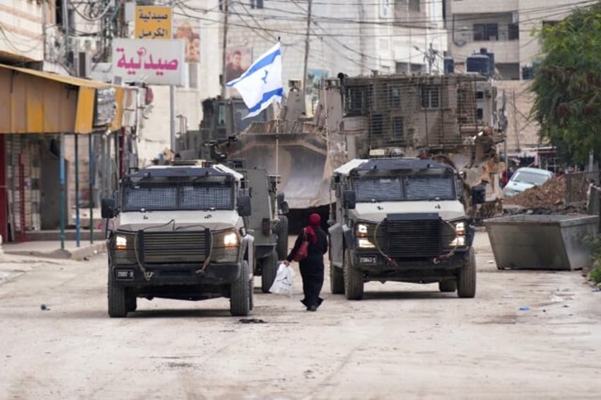 A Palestinian woman walks past Israeli army vehicles during a military raid in Jenin in th