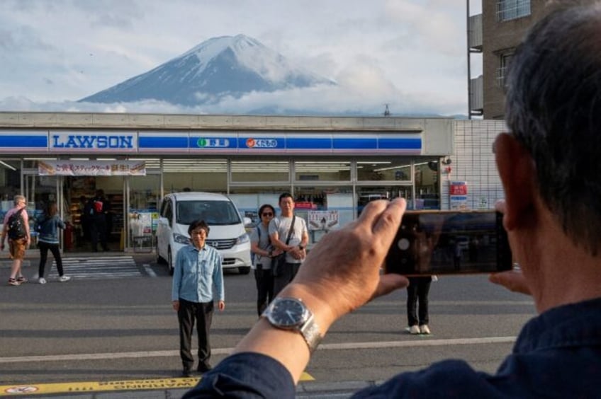 Tourists take pictures of Mount Fuji from opposite a convenience store in the town of Fuji