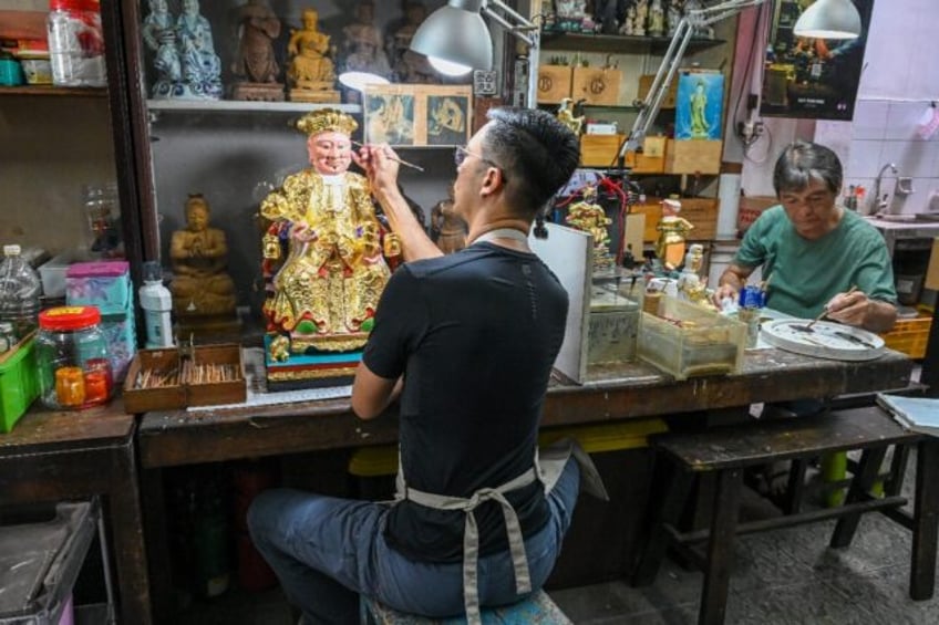 Singaporean artisan Ng Tze Yong (L), and his father Ng Yeow Hua, work on Taoist deity statues at their workshop, one of the last of its kind in Singapore