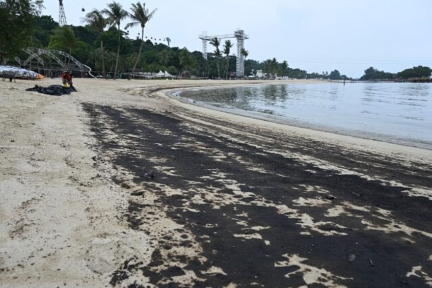 A worker clears oil slick on Sentosa island's Siloso beach in Singapore on June 15