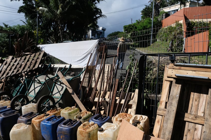 TOPSHOT - A temporary barricade, including containers of water in the event of a fire, is set up by residents with the aim of keeping watch over their neighbourhood in a peaceful manner along a road in the Magenta district of Noumea on May 16, 2024, amid protests linked to a debate on a constitutional bill aimed at enlarging the electorate for upcoming elections of the overseas French territory of New Caledonia. France ordered troops to guard ports and the international airport in its Pacific territory of New Caledonia as a state of emergency started on May 16 after two nights of riots left four dead and hundreds wounded. (Photo by Theo Rouby / AFP) (Photo by THEO ROUBY/AFP via Getty Images)