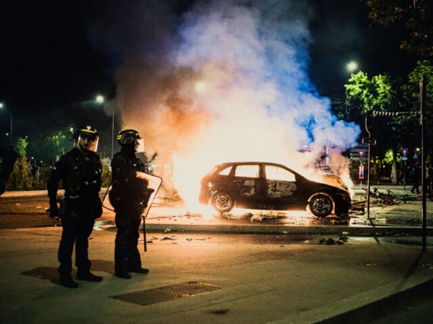 Police officers stand next to a car on fire during celebrations in the Place de la Porte d