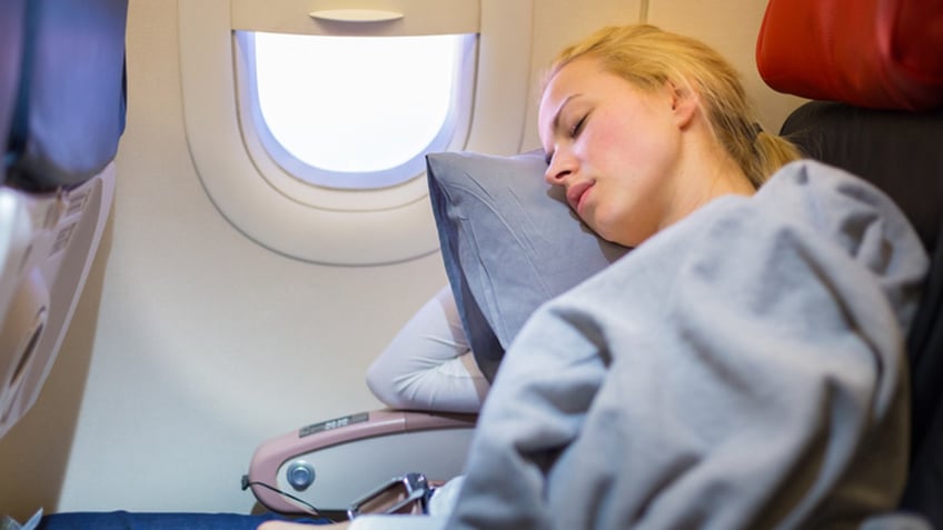 Tired blonde casual caucasian lady napping on uncomfortable seat while traveling by airplane. Commercial transportation by planes.