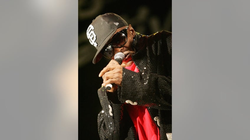 A close-up of Sly Stone wearing a hat and performing on stage.