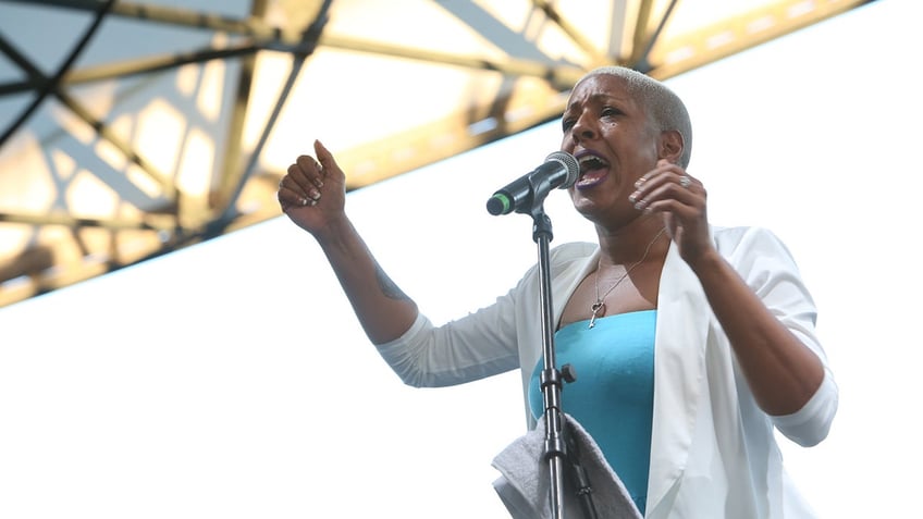 Phunne Stone performing on stage wearing a white blouse and a blue tank top.