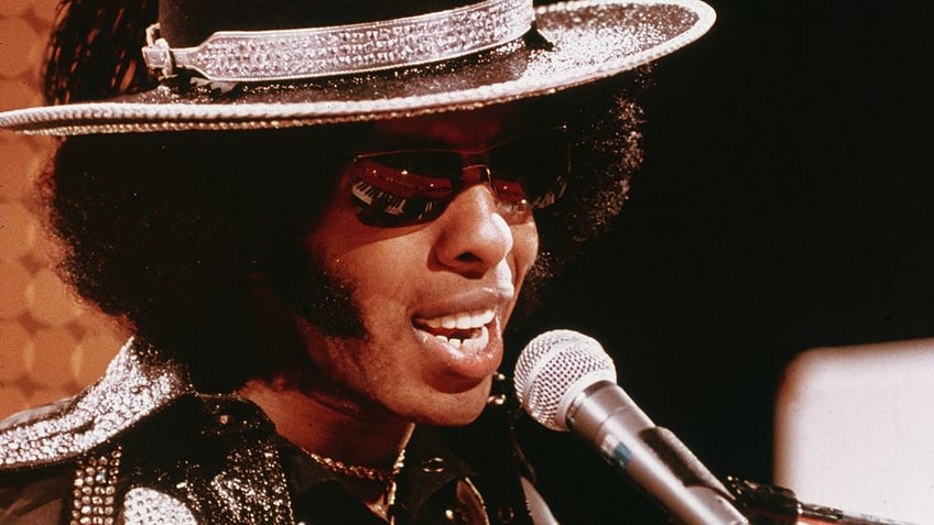 A close-up pf Sly Stone singing to the mic.