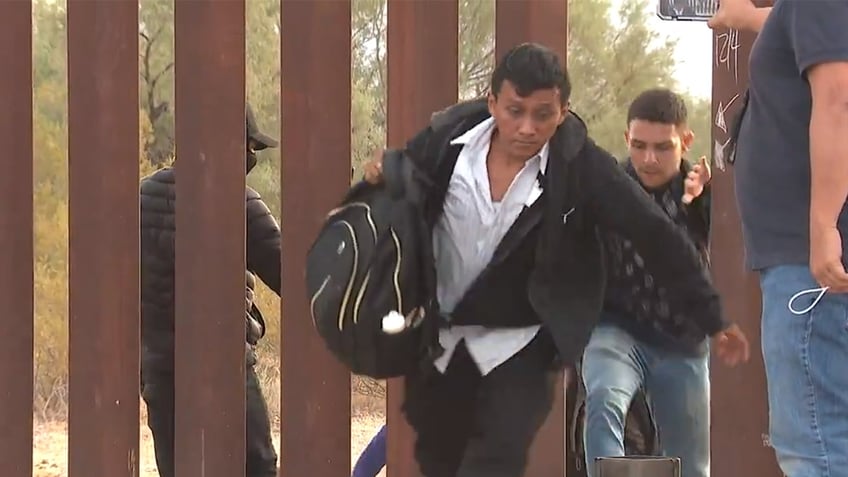 smuggler salutes camera as he leads migrants through broken section of border wall