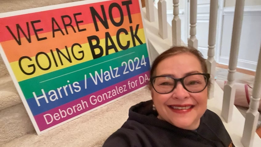 Deborah Gonzalez poses next to a rainbow-colored Harris-Walz sign