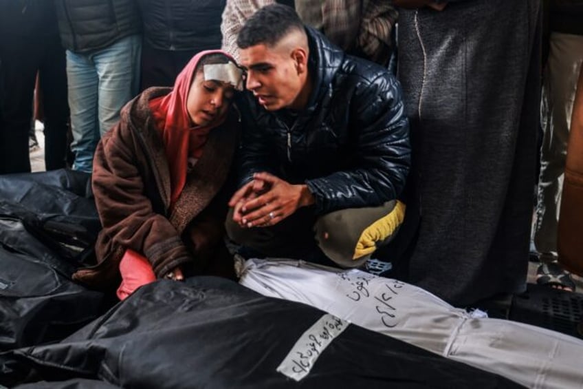 An injured girl and a man at Rafah's Al-Najjar hospital mourn over the bodies of relatives