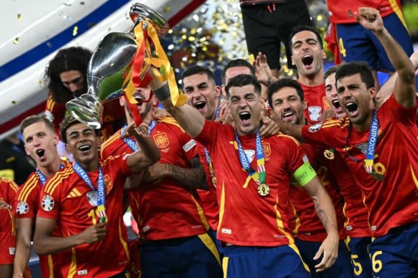 Spain skipper Alvaro Morata (C) raises the Euro 2024 trophy aloft with Rodri and Lamine Ya