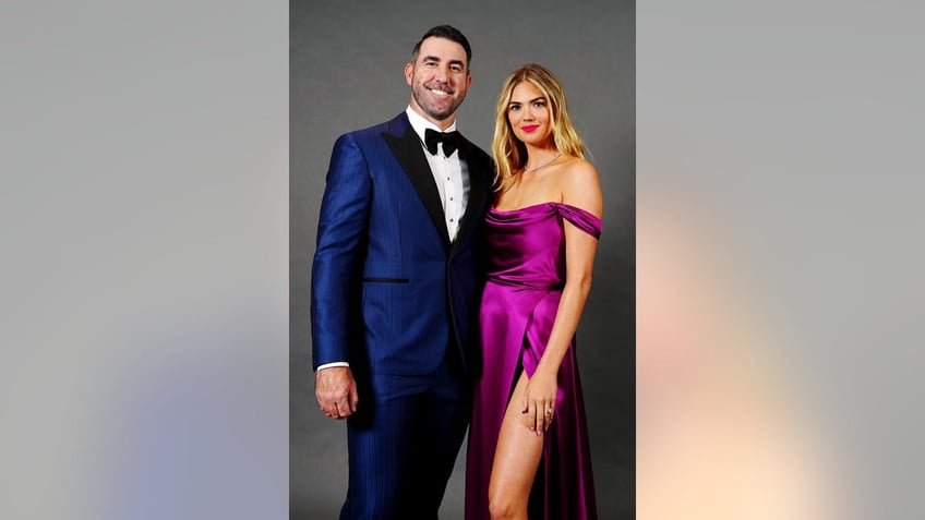 Kate Upton in a purple satin dress posing with her husband in a blue suit.