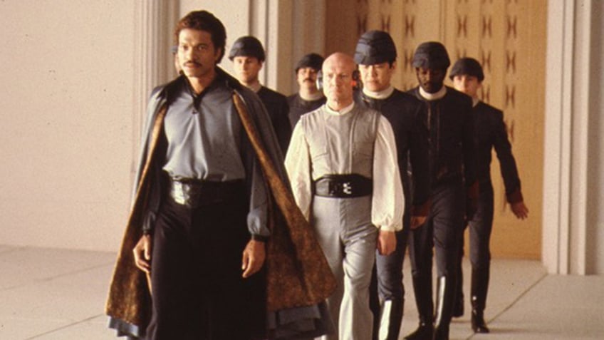 Billy Dee Williams in costume walking in front of a group of men