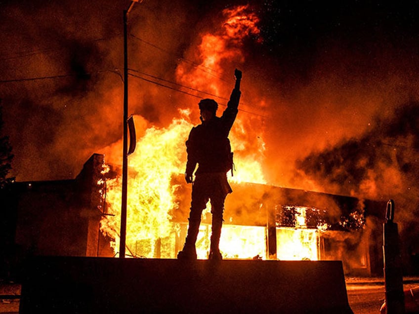 A protester reacts standing in front of a burning building set on fire during a demonstrat