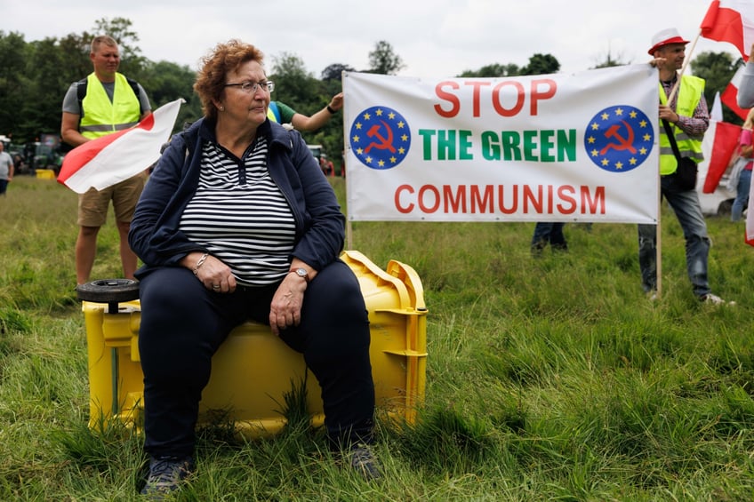 A woman sits on a bin as demonstrators hold a banner reading « stop the green communism » during a demonstration called by Farmers Defence Force to protest against European regulations, in Brussels, on June 4, 2024. (Photo by Simon Wohlfahrt / AFP) (Photo by SIMON WOHLFAHRT/AFP via Getty Images)