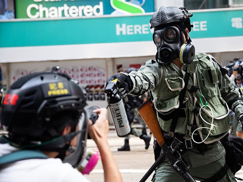 A riot police officer aims pepper spray at a journalist during a protest at Causeway Bay district in Hong Kong, China, on Sunday, Sept. 29, 2019. Hong Kong police used a water cannon, rubber bullets and tear gas on protesters who set a train station entrance on fire and hurled …